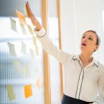 Woman in white collar shirt putting sticky notes on a board for an Asper School of Business Executive Education photo.