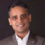 Ekram Hossain stands smiling posing for the camera against a black background.