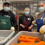 Three students in masks volunteering in a kitchen.