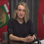 Dr. Joss Reimer at a microphone during a press conference. Manitoba flags in the background.
