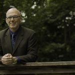 Professor Thomas Telfer leaning on a wood rail with a forest background