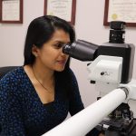 Dr. Vimi Mutalik peers into a large microscope on her office desk.