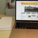 desk with a open notebook and open laptop. the screen is open to athe university of manitoba libraries webpage.