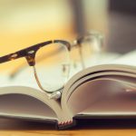 Open book with eyeglasses resting on it.