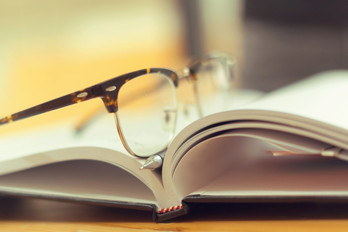 Open book with eyeglasses resting on it.
