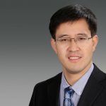 Asper professor Lei Lu wearing a black suit and tie, smiling with glasses on.