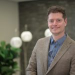 Asper student Graham Taylor smiling with a dark beige suit jacket and blue shirt on.
