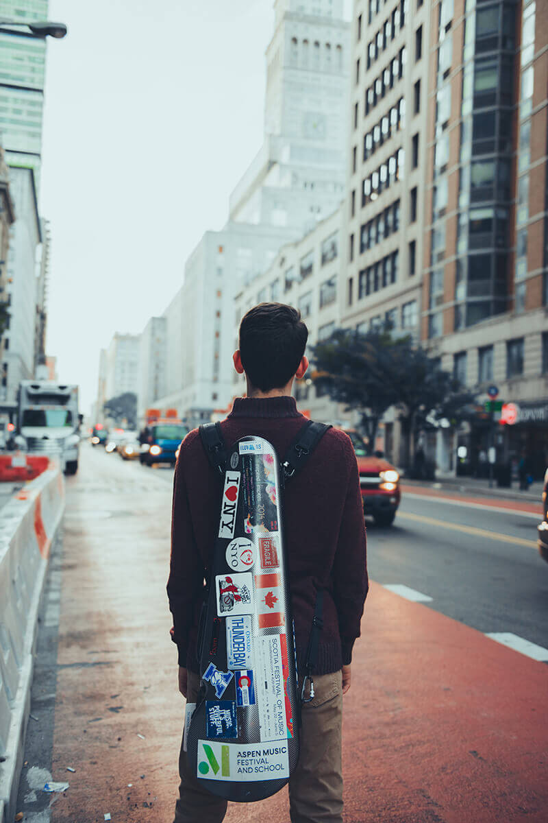 Gregory Lewis stands with his instrument case on a hazy street.