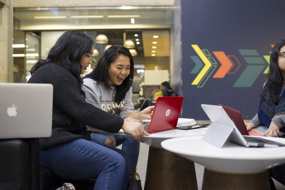 Two students look at a red laptop on a table in Campo. They are excited about what they see on the screen.