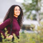 Student Awareness and Perceptions Survey Contest: A person stands smiling, with tree leaves in foreground