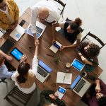 Eight business people collaborating around a table, each with a mobile device.