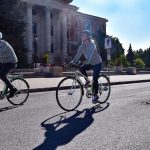 Two people cycling past the Administrative Building on a sunny day.