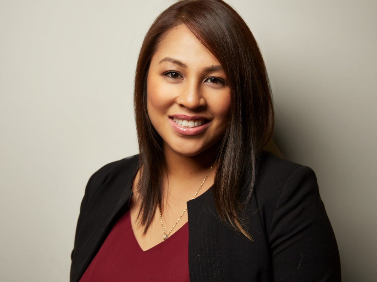 A woman, Catherine David, is smiling for her headshot wearing a red shirt and black blazer.