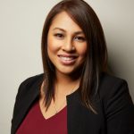 A woman, Catherine David, is smiling for her headshot wearing a red shirt and black blazer.