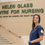 A female Indigenous nursing student stands in front of the College of Nursing building.