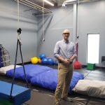 David Ambrose poses in his play therapy clinic, with gym mats and colourful balls behind him.