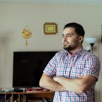 Ameen stands with his arms crossed in a living room.