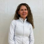 Nicole Evans standing in front of a white wall with a white sweater on.
