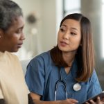 A young health-care professional of Asian descent and an elderly patient of African discuss the patient’s care while looking at a tablet computer.