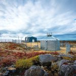 northern landscape in May with colourful foliage, set on a coast. A blue building in the background beneath a breathtaking cloudy skyline.