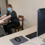 A student demonstrates physical therapy exercises in front of a computer equipped with a webcam.