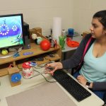 A student sits at a computer using tongs that have a wireless mouse attached.