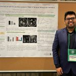 Mahamud Haque stands in front of his poster that is pinned to a bulletin board.