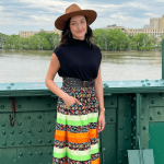 Katie McKenzie wearing a ribbon skirt standing on a green bridge overlooking the Red River.