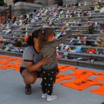 A woman who attended an Indian Day School joins her daughter as they look at the Orange shirts, shoes, flowers and messages on display outside the B.C. legislature in June 2021. THE CANADIAN PRESS/Chad Hipolito