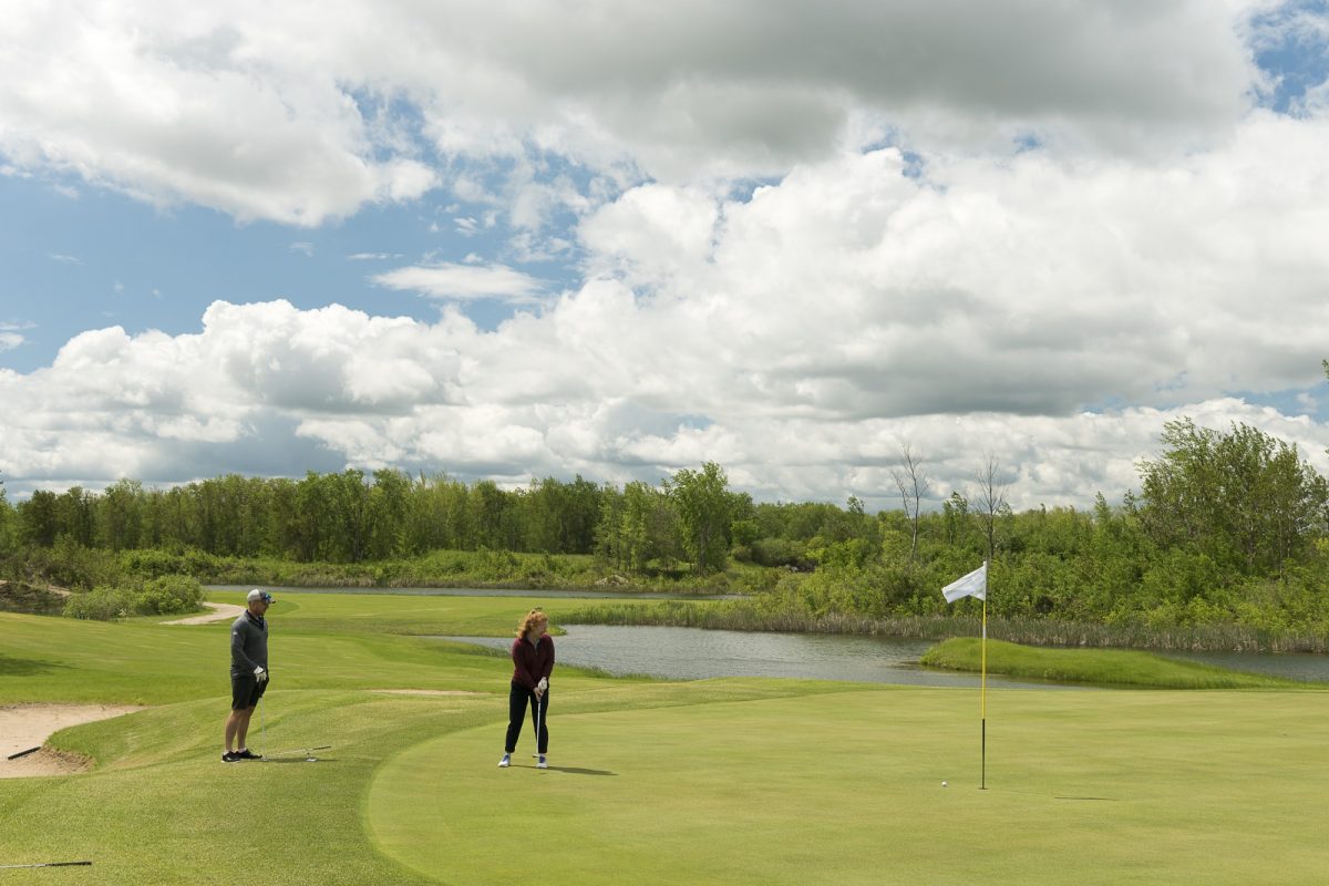 Two golfers standing on the green getting ready to putt. The sky is bright with broken cloud.