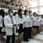 The members of the Medicine Class of 2026, all wearing white coats, stand to recite the Physician's Pledge.