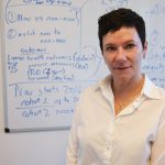 Portrait of Dr. Kathleen Decker. A whiteboard with blue writing all over it is in the background.