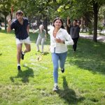 two students running forward with sticks in hand while three people cheer in the background.