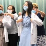 Faculty members help two dental hygiene students to don white coats at Opening Assembly.