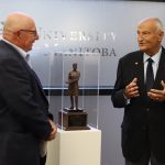Dr. Brian Postl and Gary Solar stand on either side of the sculpture while conversing.
