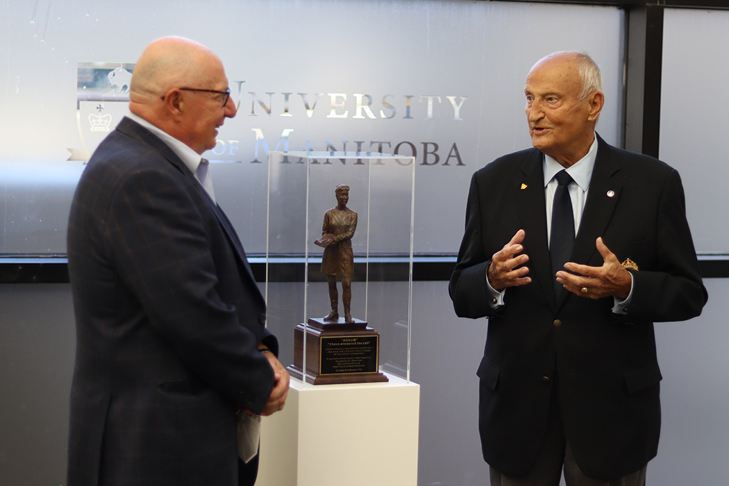 Dr. Brian Postl and Gary Solar stand on either side of the sculpture while conversing.
