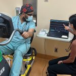 Emelissa Valcourt points to a graph on a laptop screen while Zahurul Islam sits on a stationary bike.