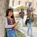 Student stands in front of Migizzi Agamik building with students in background.