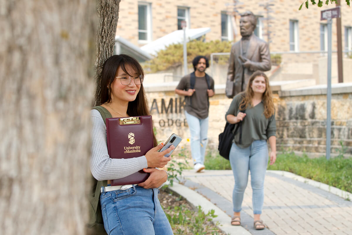 Student stands in front of Migizzi Agamik building with students in background.