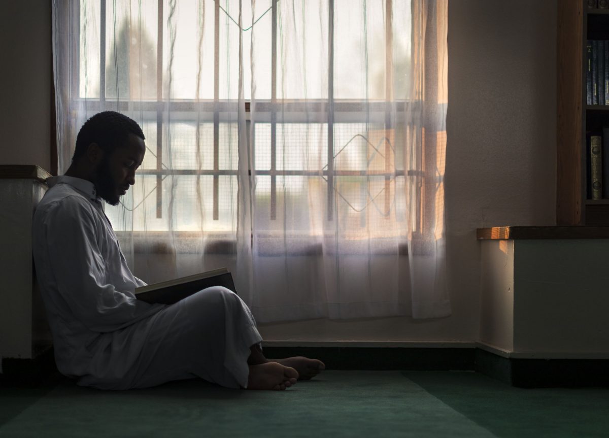 Photo by Colin Corneau showing a person sitting in quiet contemplation with a book in their lap. They sit beside a window covered with a translucent white curtain.