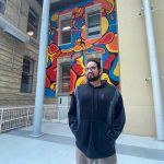 Blake Angeconeb stands in front of the mural he painted.