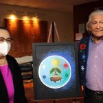 Two people stand beside an easel with art on it.