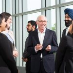 Donor Stu Clark wearing a black suit smiling and talking to Asper MBA students.