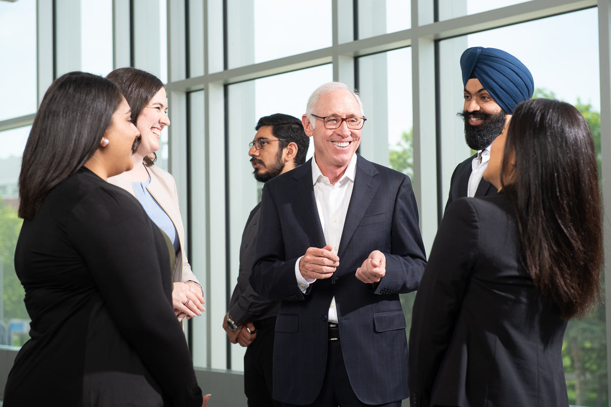 Donor Stu Clark wearing a black suit smiling and talking to Asper MBA students.