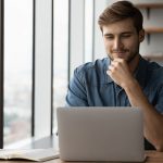 man at his laptop by an office window.