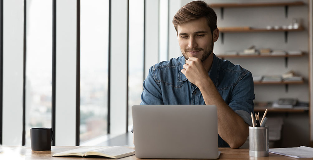 man at his laptop by an office window.