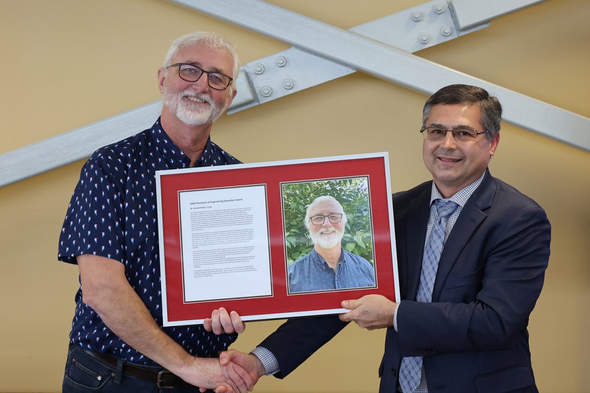 Don Petkau and Danny Mann shaking hands while holding the champion of engineering frame
