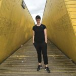 Caucasian student dressed in black stands in front of a yellow bridge