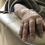 A man's arm on an armrest is attached to an IV with tubes.