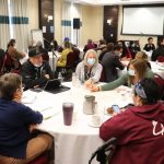 University and community representatives work at tables in a conference room.